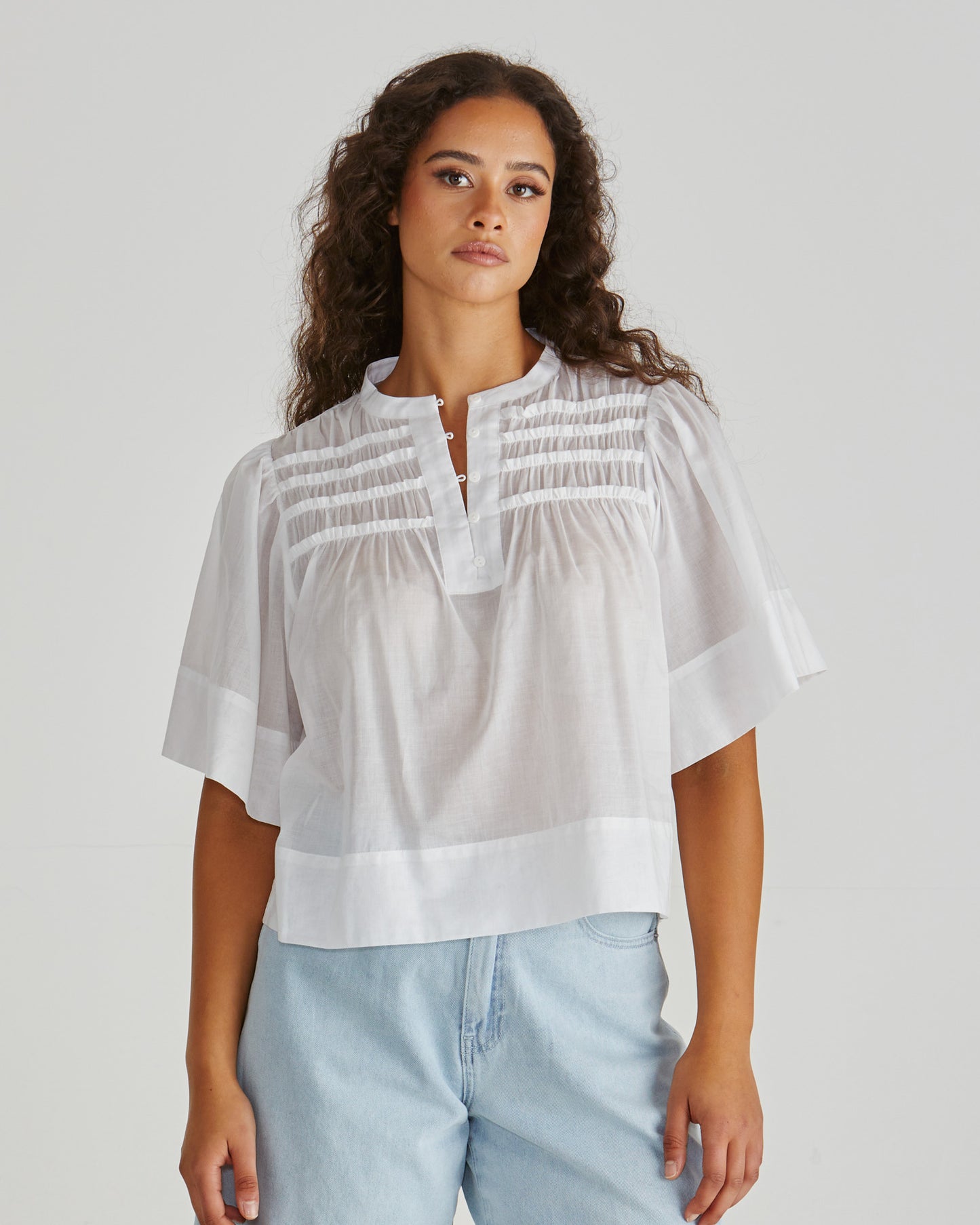 Lady wearing the SASS Pammi Blouse in white with ruffle detail, button front and wide hem. Available at Loloma Living, Tamborine Mountain. Stockist of SASS and Betty Basics.
