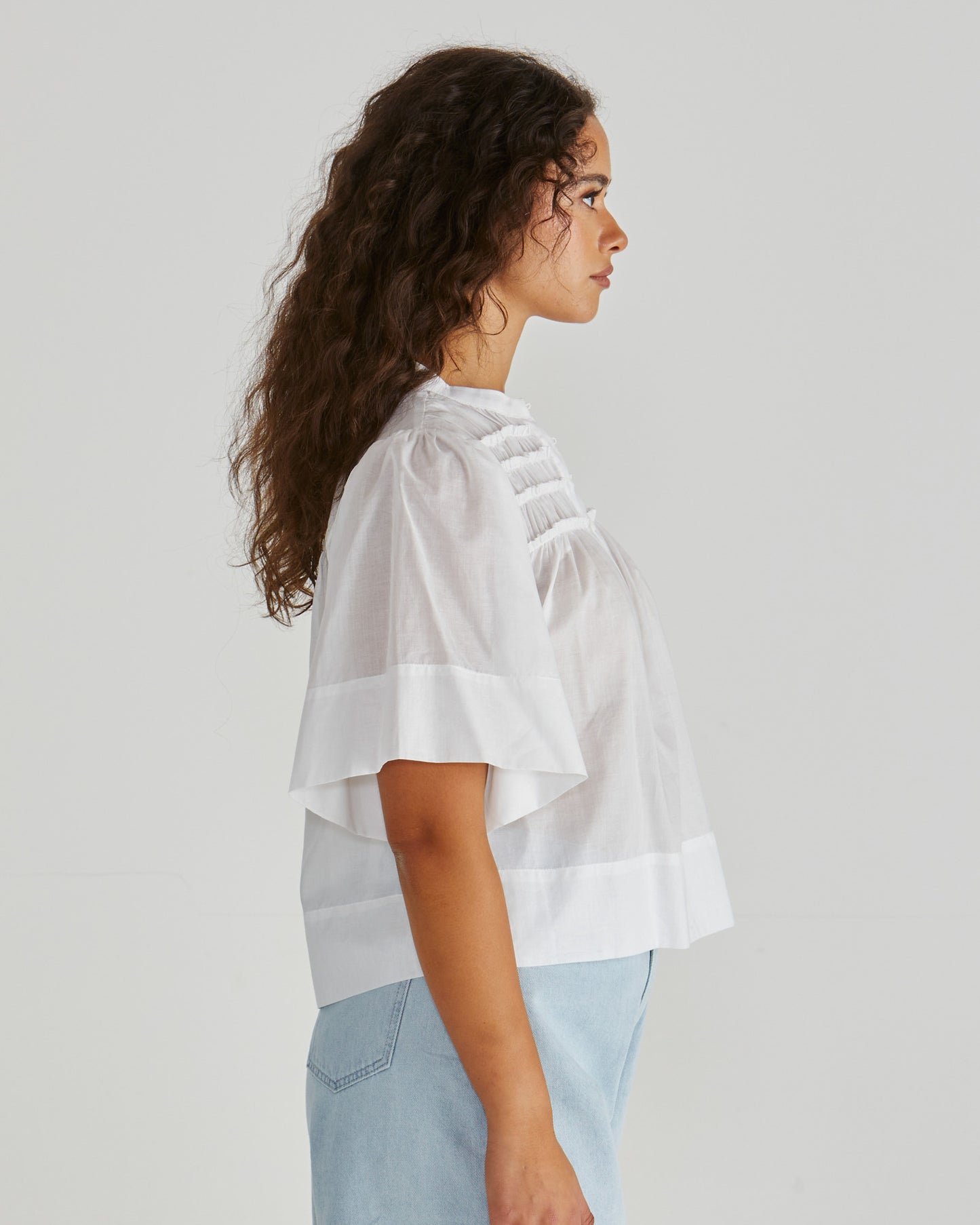 Side View of Lady wearing the SASS Pammi Blouse in white with ruffle detail, button front and wide hem. Available at Loloma Living, Tamborine Mountain. Stockist of SASS and Betty Basics.
