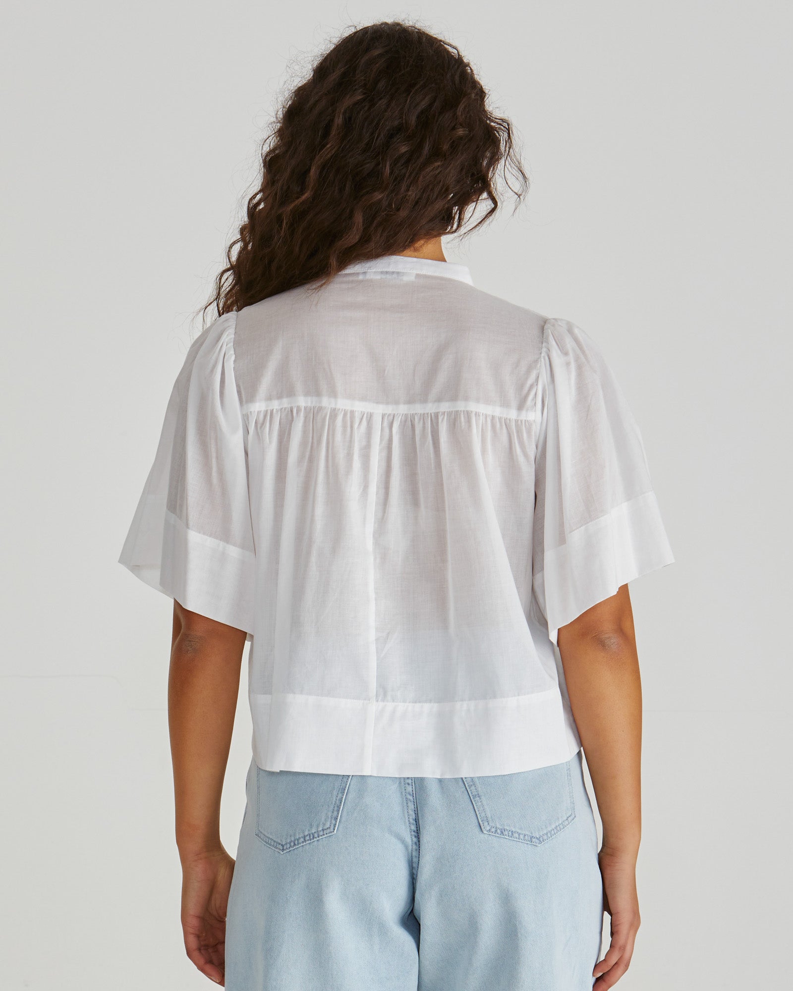 Back View of Lady wearing the SASS Pammi Blouse in white with ruffle detail, button front and wide hem. Available at Loloma Living, Tamborine Mountain. Stockist of SASS and Betty Basics.
