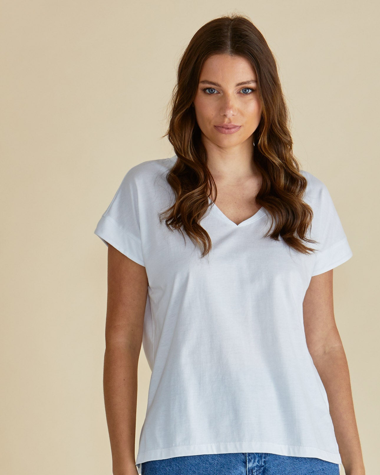Woman wearing a white t-shirt and blue jeans against a beige background