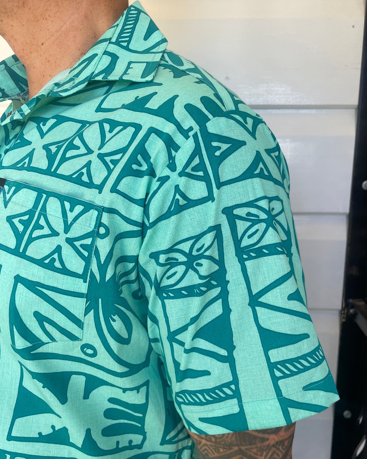 man wearing island shirt with pacific print in teal colour showing a close up of the sleeve and collar. Available at Loloma Living, Tamborine Mountain.